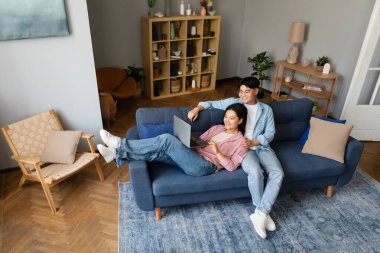 İnternette dizüstü bilgisayar kullanan Koreli çift hafta sonları evlerinde kanepede birlikte oturup dinleniyorlar. Modern Yaşam Tarzı, Bilgisayar Kullanıcıları İnternet Konseptini Tarıyor. Yüksek Açı Görünümü