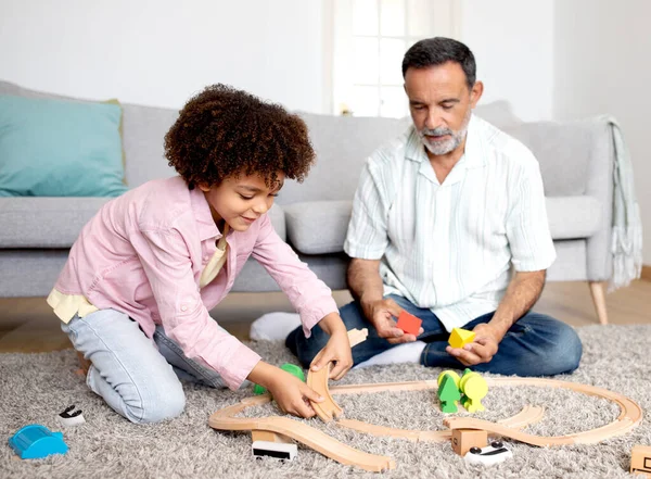 与祖父的游戏时间 快乐的西班牙裔爷爷和小孙子在家里玩玩具 坐在客厅的地板上 有选择地关注孙子女男孩 — 图库照片