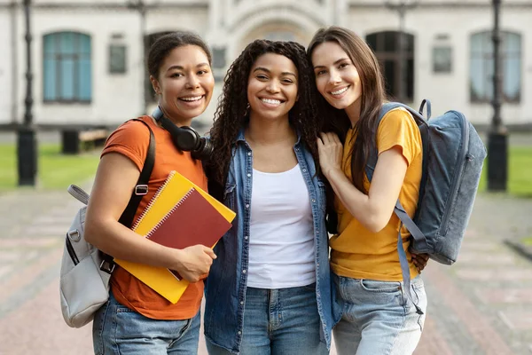 Three Happy Female Students With Backpack And Workbooks Posing Together Outdoors, Cheerful Young College Friends Standing At Campus, Embracing And Smiling At Camera, Closeup Portrait