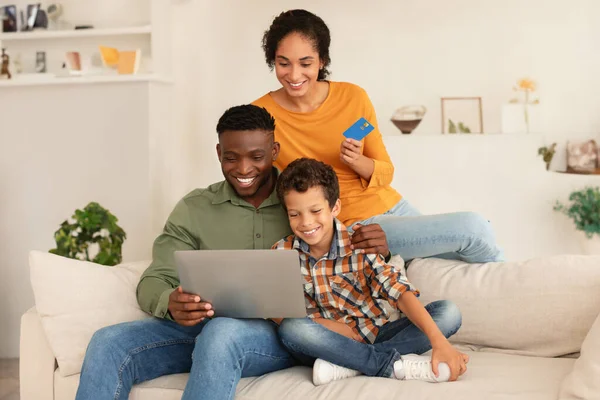 家庭网上购物 多种族父母和小男孩使用笔记本电脑和信用卡 通过网上银行购物和付款坐在沙发上在家 网店客户 — 图库照片