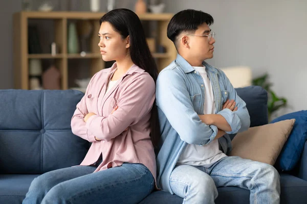 Family Conflict. Unhappy Asian Spouses Sitting On Couch Back To Back Sulking After Quarrel At Home, Looking At Different Sides, Suffering From Disagreement, Indifference And Relationship Problems