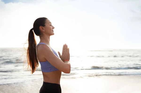 Calm glad young caucasian woman enjoy morning workout alone, silence, calm and breathing exercises, practicing yoga on sea beach. Meditation, sports, lifestyle and body care outdoor