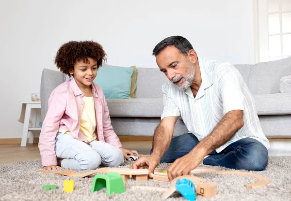 代代相传的游戏时间 笑笑西班牙裔爷爷和小孙子享受玩具乐趣 在现代客厅里玩耍和粘合 坐在家里的地板上 — 图库照片