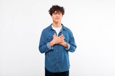 Sevgi ve İyilik. Barışçıl bir adam göğüs göğse, dilek diliyor ve dua ediyor. Gözleri kapalı beyaz stüdyo arka planında duruyor. Minnettar genç adam kalbine dokunuyor ve şükranlarını sunuyor.