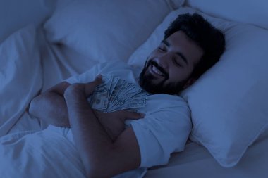Geceleri elinde dolarla dolaşan gülümseyen Hintli adam, sakin sakin Doğu erkeği zenginliği ve zenginliği hayal eden, para banknotlarını tutan, karanlık yatak odasında kestirirken,