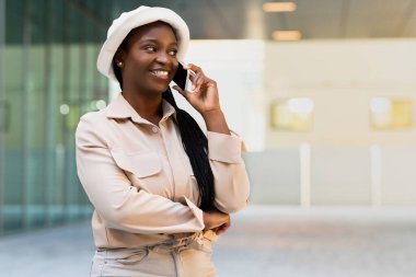 Şık giyinmiş mutlu, genç, siyah bir kadın sokakta telefon görüşmesi yapıyor. Afro-Amerikan öğrenci akıllı telefondan konuşuyor ve gülümsüyor. İletişim konsepti