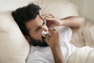 Hasta Hintli genç adam, evde yatarken kağıt mendile burun sümküren, Doğu 'lu hasta, migren ağrısı çeken, mevsimsel grip veya soğuk algınlığı olan, Rhinitis veya Alerjik reaksiyon gösteren,