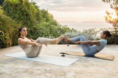 Ciddi ciddi bin yıllık siyahi, beyaz kadınlar egzersiz yapıyor, bir şişe suyla birlikte yoga yapıyorlar, sabah dışarıda antrenmanların tadını çıkarıyorlar. Parklarda yaşam tarzı, sağlık ve kilo kaybı