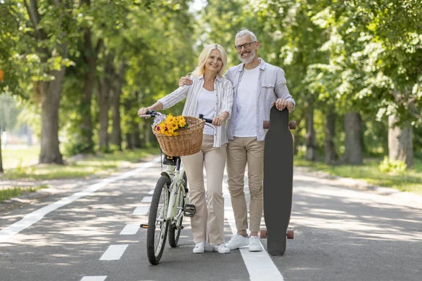 具有自行车和滑板的现代老年人在城市公园中的肖像 快乐成熟的男人和女人享受着主动退休的快乐 骑自行车和长期户外的快乐 看着相机微笑 — 图库照片