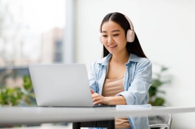 Çevrimiçi çalışma. Neşeli Asyalı bayan dizüstü bilgisayar kullanıyor, klavyede daktilo kullanıyor, online ders veya webinar izliyor, üniversite seyircilerinin arasında oturuyor. Dişi sörf ağı ve öğrenme, ev ödevlerini evde yapıyor.