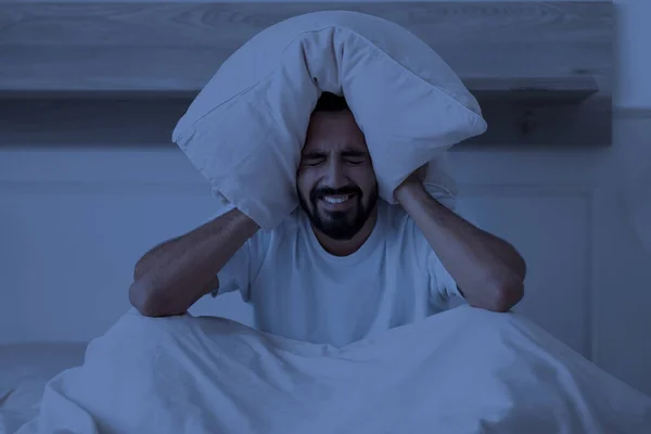 不眠症のコンセプト 夜に家でベッドで座っている間 ストレスを受けたインド人の男は 眠っている無駄な若い東部の男広場で枕で耳を覆う — ストック写真