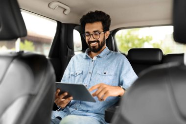 Neşeli genç doğu çocuğu havaalanına taksiyle giderken e-postaları kontrol ediyor, arka koltukta oturuyor ve dijital tablet kullanıyor, ön koltuktan çekiliyor, boşluğu kopyalıyor. Ulaşım, araba yolculuğu