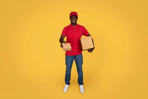 令人高兴的是 身穿制服的千年期非洲裔美国人快递员送来了盒子 快递员享受着工作 在橙色工作室背景下与世隔绝 现代职业 — 图库照片
