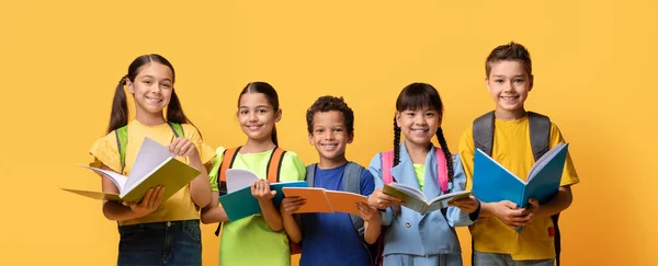 教育コンセプト 多様な学生の幸せな男の子とカメラを見ている女の子のグループ カジュアルな服を着て バックパックやエクササイズの本を運ぶ 黄色のカラースタジオの背景 バナー — ストック写真