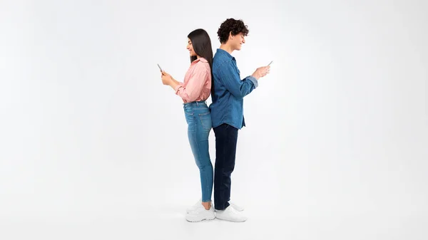 接続されたオンライン 幸せな学生の若いカップルは 携帯電話を使用して ソーシャルメディア テキストとブラウジングウェブを自分のスマートフォンに取り入れ ホワイトバックグラウンドでスタジオに戻ります パノラマ — ストック写真