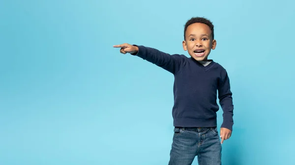 stock image Funny african american boy pointing aside at copy space, emotional male child demonstrating free place for advertisement, standing isolated over blue background, panorama