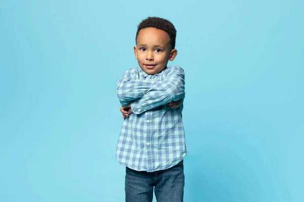 一个高兴的黑人小男孩的画像 他抱着胳膊站在那里 看着摄像机 可爱的非洲裔美国男孩在蓝色的工作室背景上摆姿势 复制空间 — 图库照片
