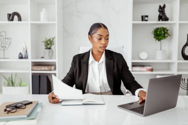 Resmi olarak çekici siyah kadın menajer dizüstü bilgisayarla masada oturuyor ve evrakları kontrol ediyor, ofiste çalışan kadın girişimci, kopyalama alanı.
