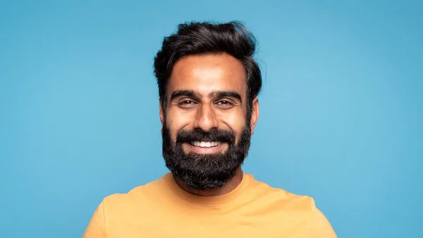 青いスタジオの背景をポーズするカメラでカジュアルに笑顔で幸せな中年のインド人男性のクローズアップ肖像画 白い歯 パノラマを示しています 男性の肖像コンセプト — ストック写真