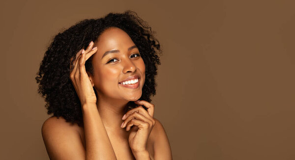 Aesthetic medicine and cosmetic surgery concept. Cheerful attractive young black woman with curly hair and perfect skin posing topless over brown studio background, copy space, banner