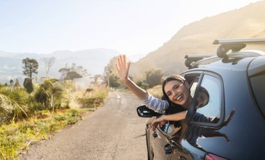 Otomobilin ön koltuğunda oturan mutlu, genç bir kadın, arabanın camından el sallıyor ve gülümsüyor. Aile, arkadaşlar, birlikte yaz tatiline çıkan çift, güzel bir hafta sonu, güneşli bir hava.