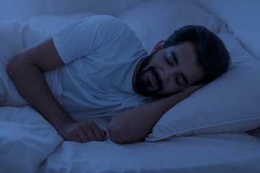 Sağlıklı Uyku Konsepti. Genç Hintli bir adamın portresi. Gece gözleri kapalı yatıyordu. Sakin doğu erkeği yatak odasında dinleniyordu.