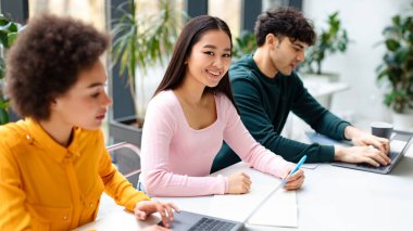 Çalışma süreci. Masada oturan çeşitli sınıf arkadaşları, üniversite sınavlarına, sınıfa ya da çalışma alanına hazırlanırken kameraya gülümseyen Asyalı bayan, panorama