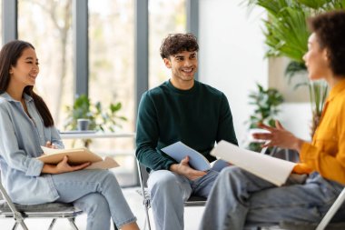 Mutlu çok ırklı öğrenci arkadaşlar birlikte eğitim projelerini konuşuyor ve tartışıyorlar, ligth modern sınıfında oturuyorlar daire şeklinde sandalyeler üzerinde.