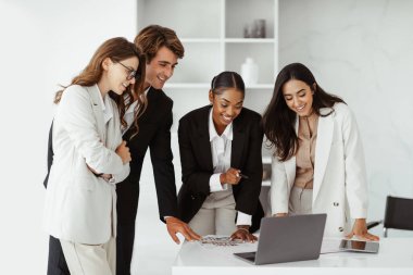 Uluslararası iş arkadaşları modern ofiste masa başında dizüstü bilgisayar kullanıyorlar, proje üzerinde birlikte çalışıyorlar, iş hedeflerini tartışıyorlar.