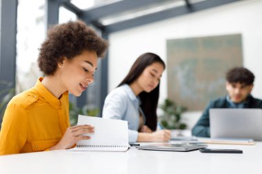 Neşeli Latin kız öğrenci sınıf arkadaşlarıyla ders çalışıyor, egzersiz kitabını okuyor, final sınavına hazırlanıyor, üniversite ödevi üzerinde çalışıyor.