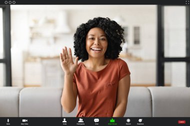 Mutlu siyahi kadın evde video görüşmesi yapıyor, kameraya el sallıyor, kamerada Afro-Amerikan kadının gülümseyen görüntüsü var, telekomünikasyonun keyfini çıkarıyor, birini selamlıyor.