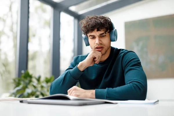 European guy listening online lecture and doing his home assigment looking attentively in copybook, writing info while sitting in university audience, free space