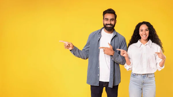 素晴らしいセールスオファー ポジティブなアラブカップルは カメラに笑顔を指し 黄色の背景 広告バナーにスタジオのコピースペースを示しています この概念をチェックしてください パノラマ — ストック写真