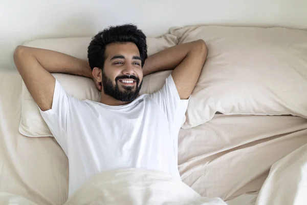 早上放松 一个英俊的印度人醒来后躺在舒适的床上笑着 一个快乐的千禧年东方小伙子在卧室休息 享受国内周末 上面有复制的空间 — 图库照片