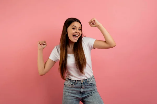 ホーリー オーバー楽しい十代の少女は ひざまずいた拳を震え 追いかけ 喜びの成功 ピンクのスタジオの背景の上に立っている間 勝利を祝う幸せな興奮した女性ティーンエイジャー コピースペース — ストック写真