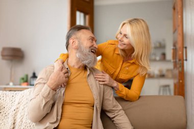 Mutlu, olgun bir çift, aşklarının tadını çıkartıyor ve uzun süreli evliliklerinin tadını çıkarıyor, kocasını seven bir eş, o oturma odasındaki koltukta otururken, kocasını kucaklıyor.