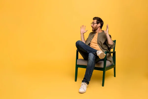ショックを受けた中年の男性は 黄色いスタジオの背景の上に椅子に座っている空きスペースを見ながら驚きで口を開きます Omg 衝撃的なニュース オファーのコンセプト — ストック写真