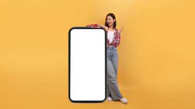 Harika bir cep telefonu. Kocaman bir cep telefonuna yaslanan mutlu Asyalı kadın boş ekran ve bağırarak Vay canına, sarı arka plan, panorama ve pankartın üzerinde tek başına duran kadın