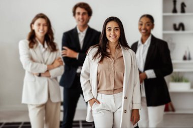 Latin iş kadını lideri, çok ırklı iş ekibiyle birlikte ofis içinde poz veriyor ve kameraya gülümsüyor, üniversiteler birlikte destek, takım çalışması ve işbirliği yapıyor.