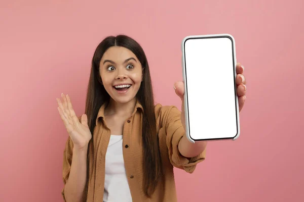 令人惊奇的报价 兴奋的少女拿着白色的空屏幕展示手机 欢呼雀跃 惊讶的年轻女子欣赏着新的应用程序 站在粉红的工作室背景 — 图库照片
