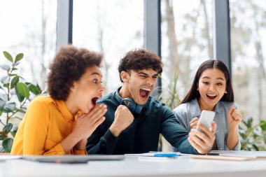 Duygusal aşırı keyifli grup arkadaşları cep telefonlarına bakıyor, yumruklarını sıkıyor ve evet diye bağırıyor, sınav sonuçlarını internetten kontrol ediyor, üniversite sınıfında oturuyor.