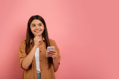 İlginç bir teklif. Dalgın Genç Kız Akıllı Telefon Tutuyor ve Çeneye Dokunuyor, Gülümseyen Kadın Meraklı Genç Yeni Mobil Uygulamayı veya Web Sitesini Düşünüyor, Pembe Arkaplanda Duruyor, Boşluğu Kopyala