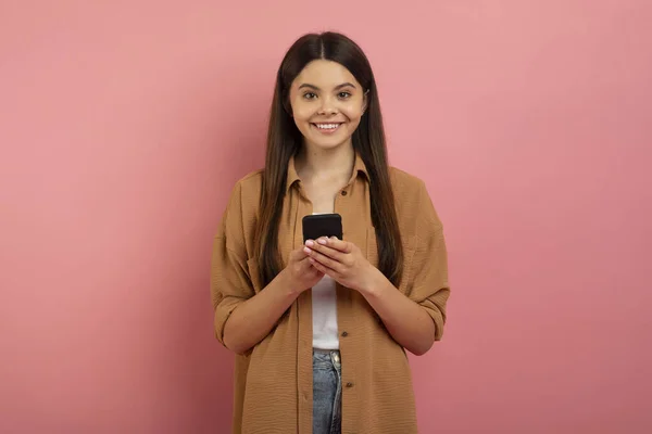 在工作室 快乐可爱的女性青少年在手机上浏览新应用程序或与朋友聊天 复制空间中手持智能手机站在粉色背景下的少女形象 — 图库照片