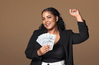 Büyük şans. Heyecanlı Brezilyalı büyük ölçekli iş kadını elinde para hayranı ve el kol hareketi yapıyor. Evet, kameraya gülümsüyor, iş başarısını ve kahverengi arka plandaki maaş artışını kutluyor.