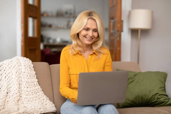 Gülümseyen Beyaz Olgun Bir Kadın Dizüstü Bilgisayarda Yazıyor Oturma Odasında — Stok fotoğraf