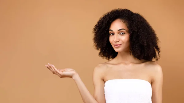 Adのための場所 美しいラテン語の女性は彼女の空のヤシで何かを宣伝し 茶色の背景にタオルで包まれた新しい美容製品をお勧めします フリースペース — ストック写真