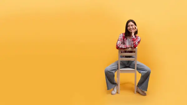 笑着坐在椅子上的年轻的中国女士在黄色的背景 工作室 全景与自由自在的空间 伟大的广告 良好的心情 休息和放松 孤独和生活方式 — 图库照片