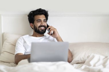 Akıllı telefonlu ve dizüstü bilgisayarlı yakışıklı Hintli adam yatak odasında dinleniyor, Milenyum boyu gülümseyen Doğulu adam evde oturuyor, bilgisayar kullanıyor ve keyifli telefon konuşmalarının tadını çıkarıyor, boşluğu kopyalıyor.