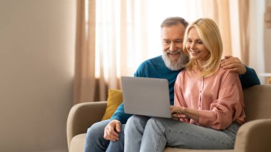 Joyful Senior Couple Video Calling Using Laptop, Communicating With Distant Family And Friends Online Sitting on Sofa At Home, Panorama With Copy Space. Internet And Remote Communication Concept clipart