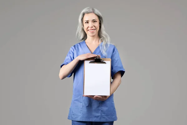 Sonriente Señora Doctora Mediana Edad Uniforme Azul Mostrando Portapapeles Vacío —  Fotos de Stock